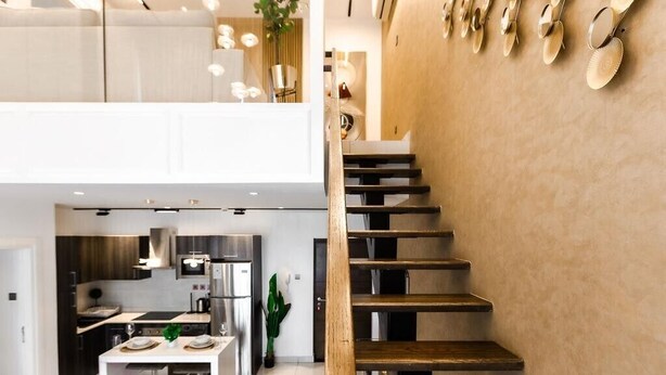 A modern kitchen with a central island, a dining area with a table and chairs, and a staircase leading to an upper level. - Ebs legend white limited (Accra)