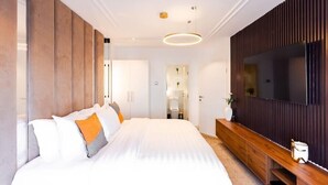 A modern bedroom with a large bed, a wooden console table, a TV, and a mirror. - Ebs legend white limited (Accra)