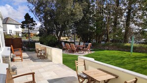 Un patio con mobiliario exterior, suelo de piedra y césped bien cuidado.