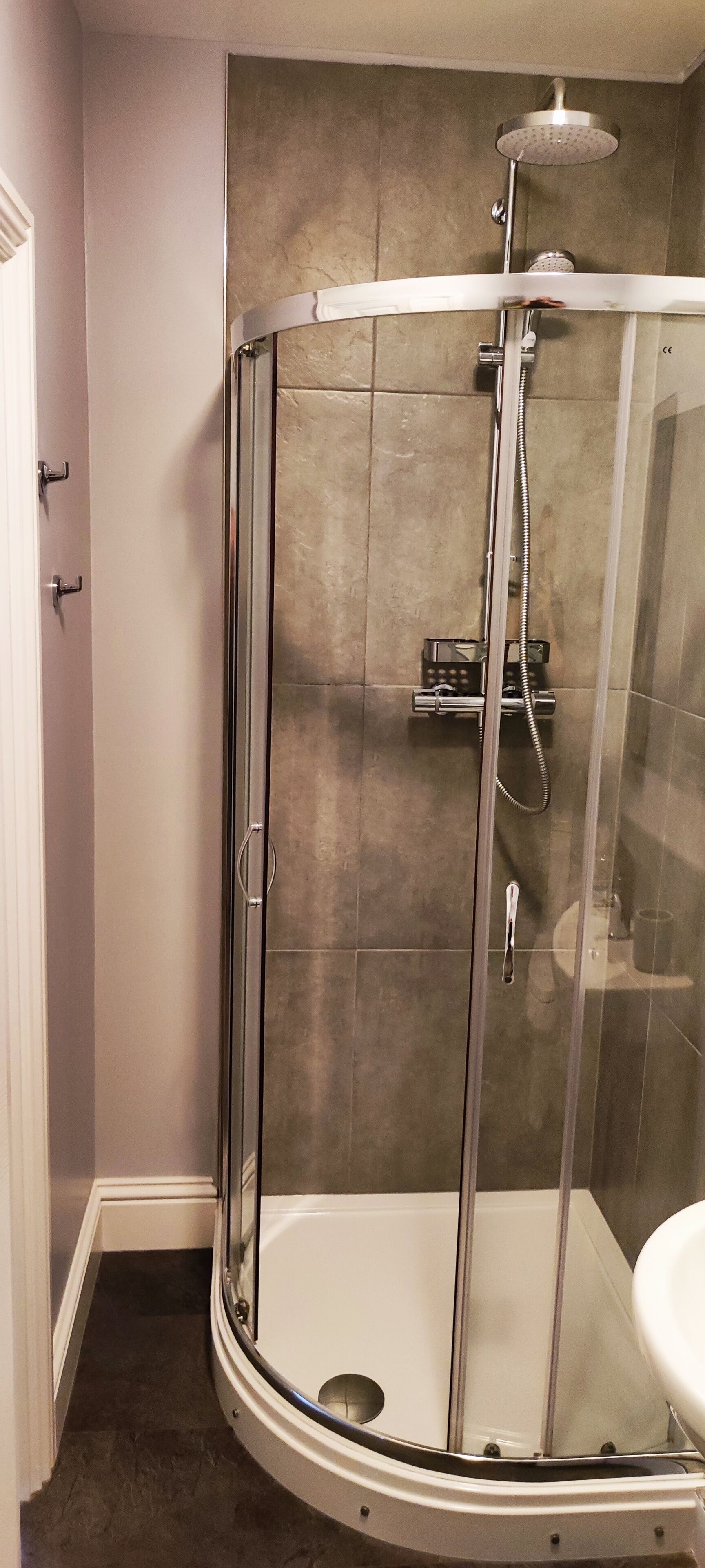 A corner shower with a glass enclosure, a white sink, and a towel rack.