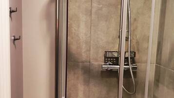A corner shower with a glass enclosure, a white sink, and a towel rack.