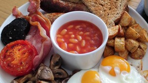 Un plato de desayuno con huevos, tocino, salchichas, champiñones, frijoles, tostadas y patatas ralladas.