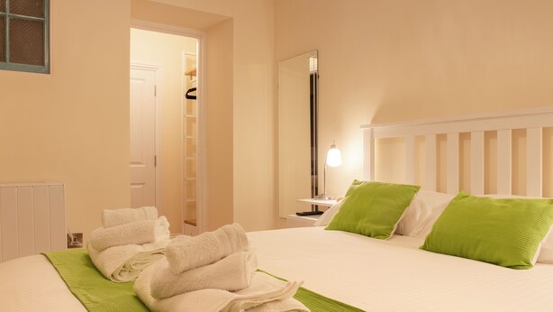 Una habitación de hotel con una cama bien hecha, una mesita de noche con lámpara, un espejo y una manta verde.