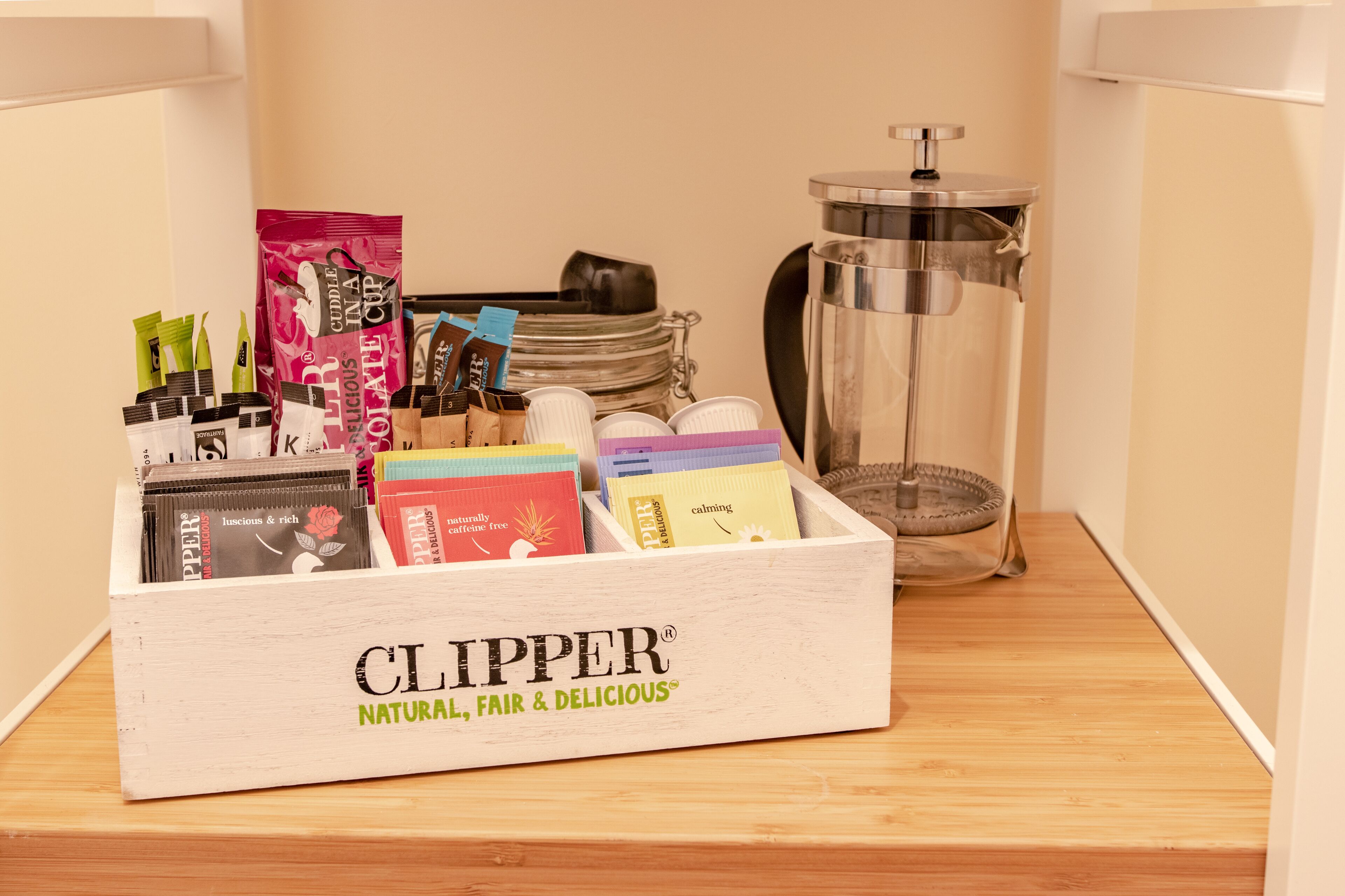 Una caja de madera con la etiqueta 'CLIPPER NATURAL, FAIR & DELICIOUS' que contiene varias bolsitas de té y un molinillo de metal.