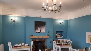 Comedor con chimenea, paredes azules, sillas blancas y candelabro.