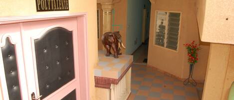 Um corredor com piso xadrez, uma porta com a inscrição "SALLE POLYVALENTE" e uma estátua de elefante.