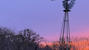 Un moulin à vent dans un champ, avec un coucher de soleil en arrière-plan.