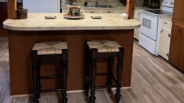 Une cuisine dotée d’un îlot central, de tabourets de bar en bois, d’un réfrigérateur blanc, d’une cuisinière et d’un lustre.