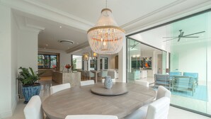Een ruime eethoek met een grote ronde tafel, witte stoelen en een decoratieve vaas in het midden.