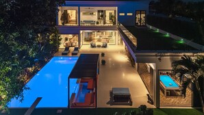 Een modern huis met twee verdiepingen, een groot zwembad, een terras en een aparte poolruimte.