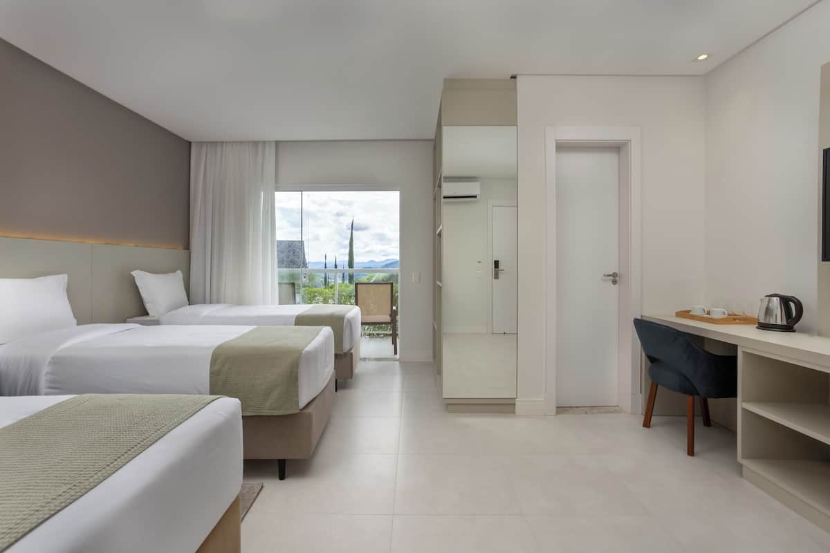 Quarto de hotel com duas camas, uma escrivaninha, uma cadeira e vista para o exterior.