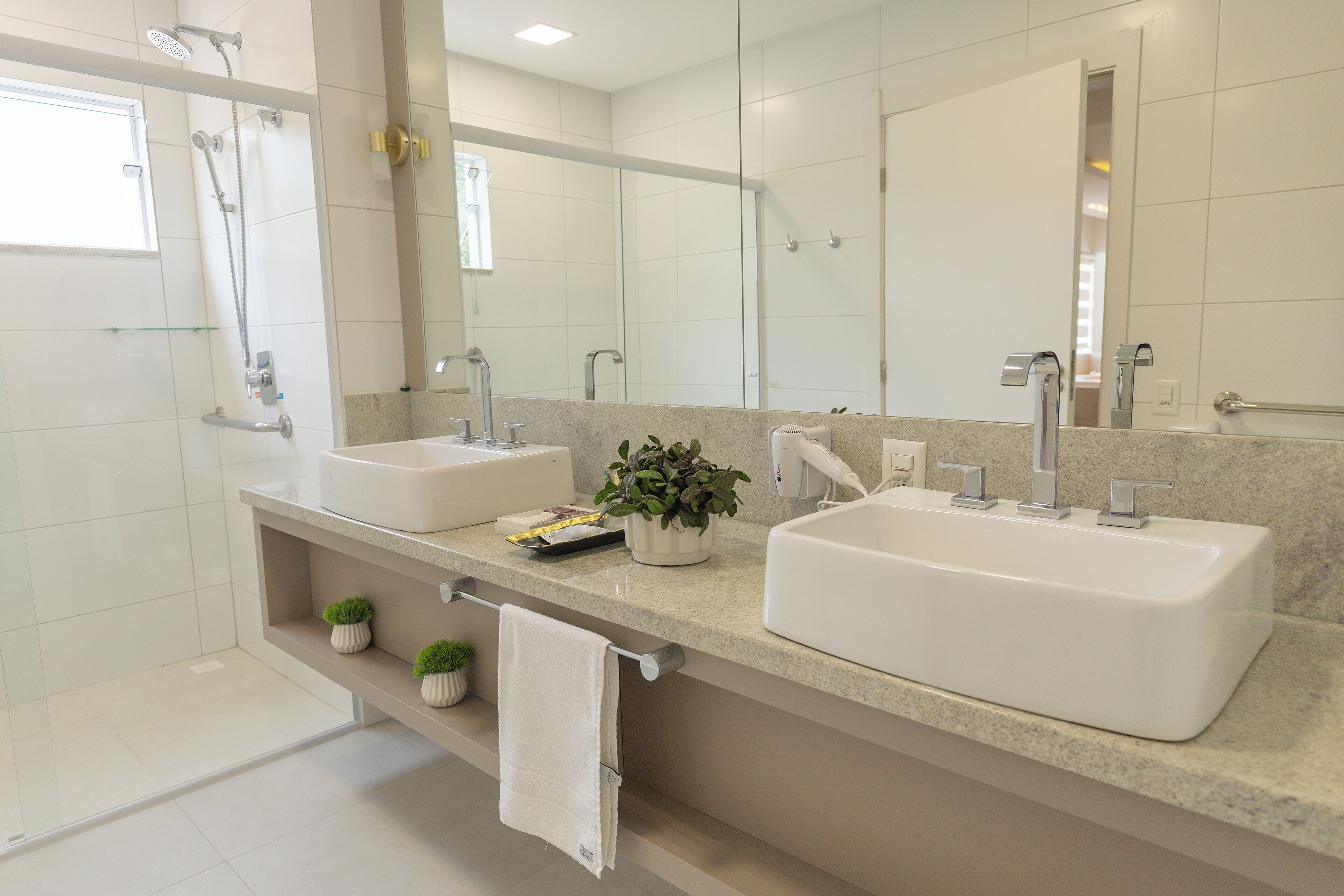A modern bathroom with two sinks, a large mirror, a shower, and a small plant on the counter.