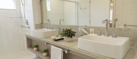 A modern bathroom with two sinks, a large mirror, a shower, and a small plant on the counter.