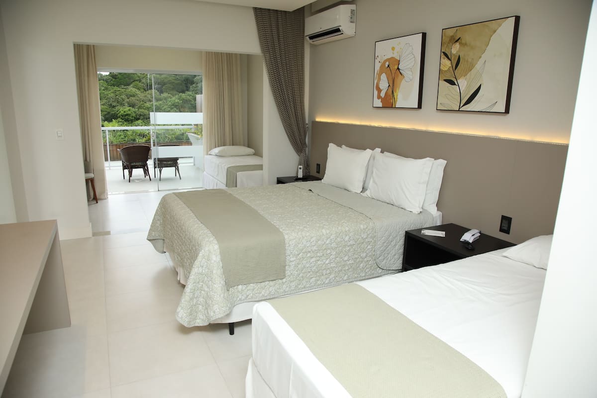 Quarto de hotel com uma cama grande, mesa de cabeceira, cadeira e varanda com vista para o verde.