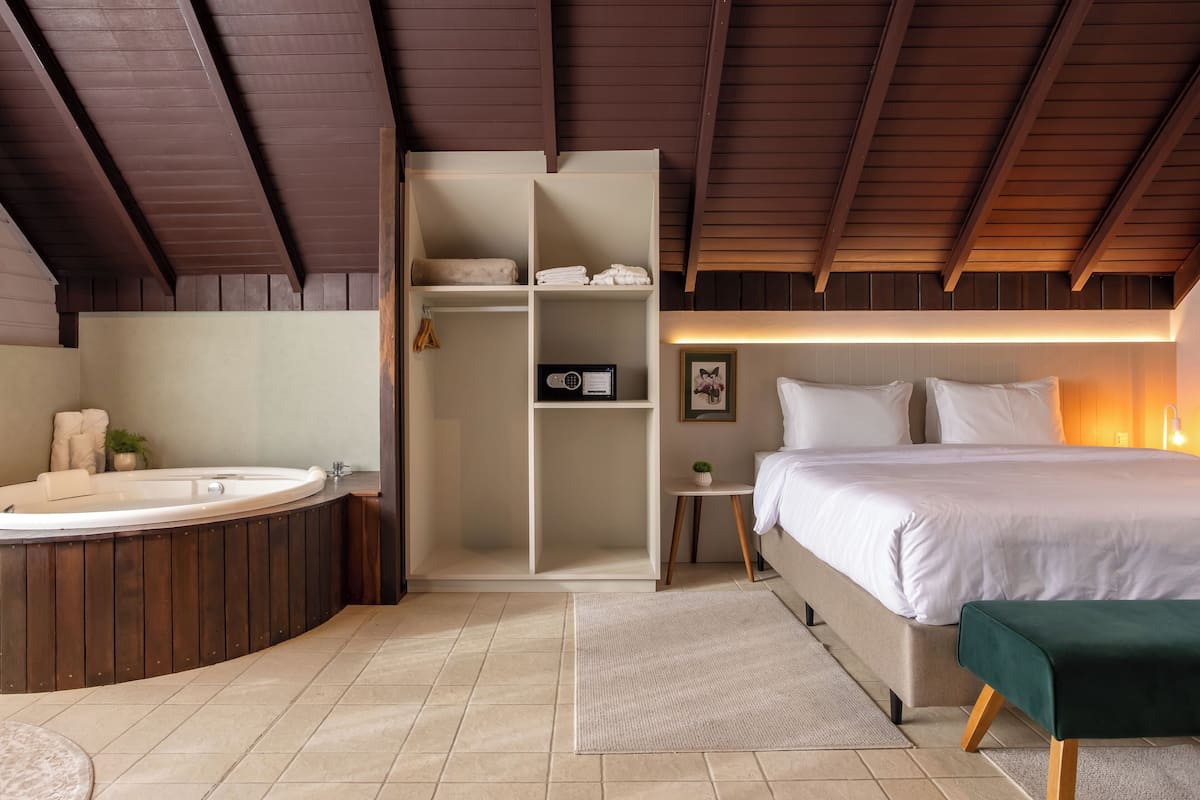 Quarto com uma cama grande, mesa de cabeceira, armário embutido, banheira e uma janela pequena.