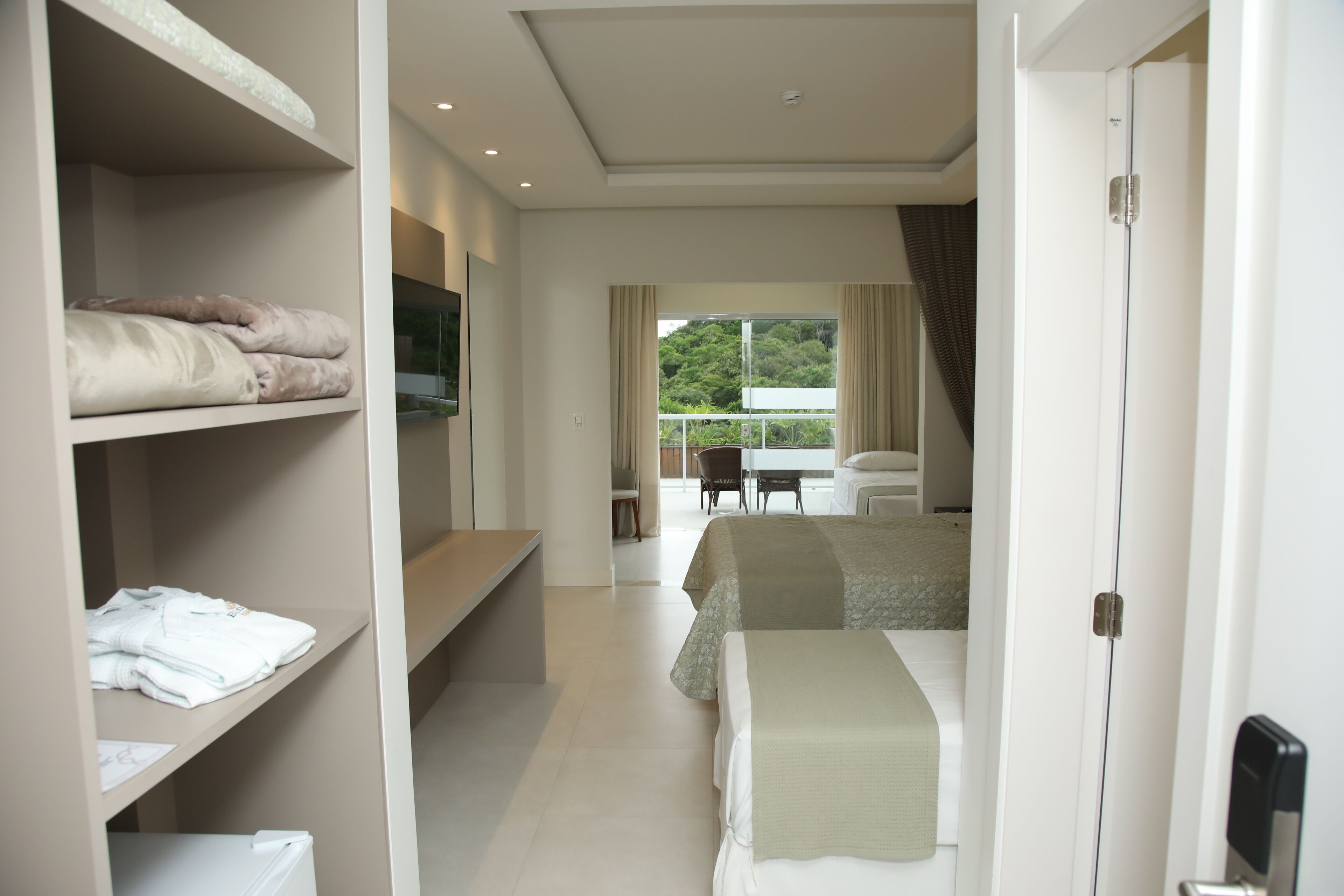 Habitación de hotel con cama, escritorio y armario. Tiene un balcón con vista a árboles.