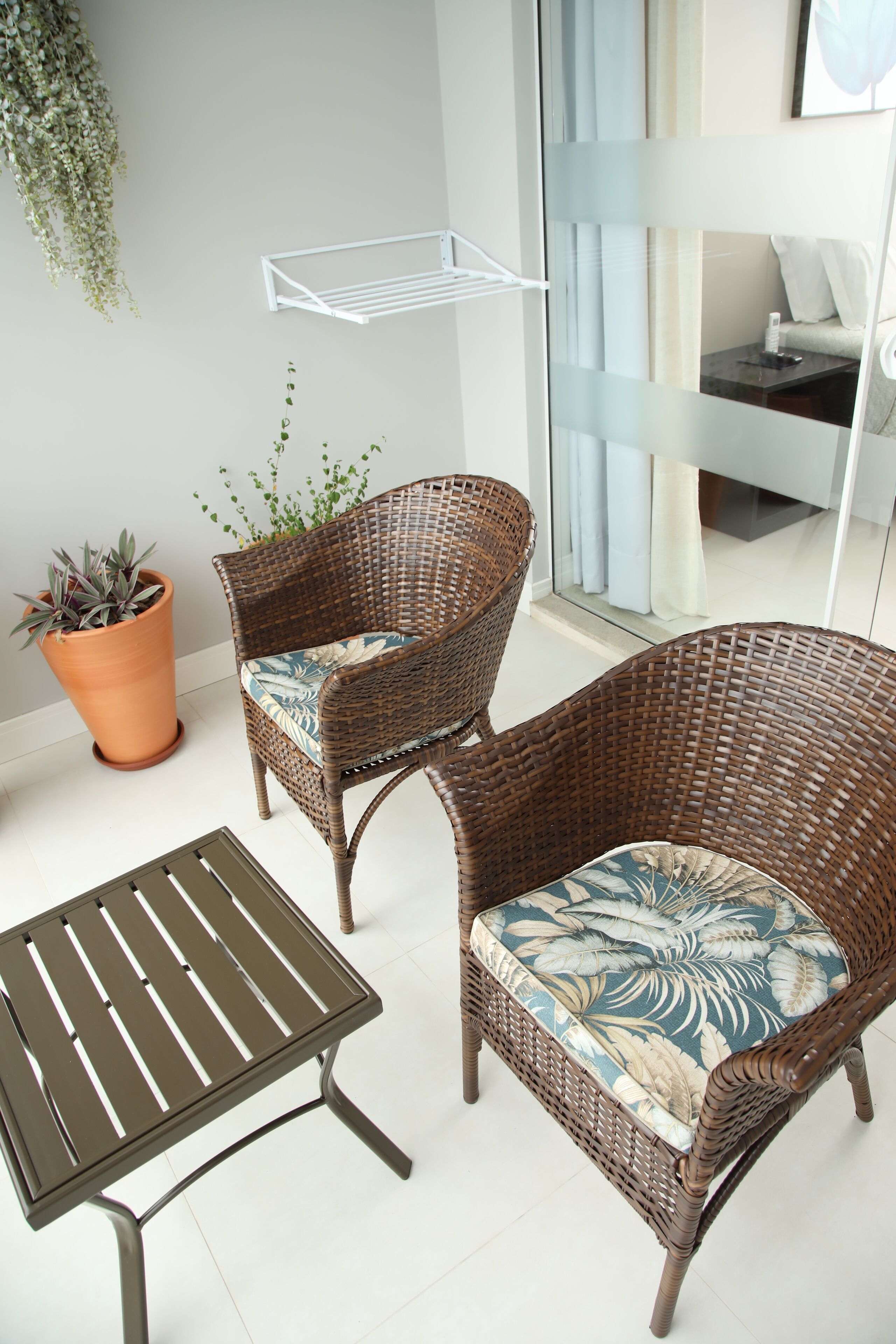A wicker chair with a floral cushion, a metal table, and a terracotta pot with a plant.