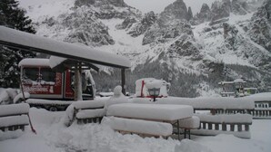 Un espacio al aire libre cubierto de nieve, con un edificio rojo y blanco, posiblemente un restaurante o cafetería, y bancos nevados.