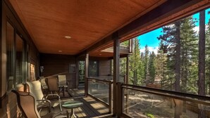 A wooden deck with chairs and tables, overlooking a forested area. - Pet Friendly + Pool Table + Shuffle Board + Arcade Game (South Lake Tahoe)