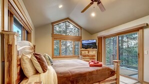 A bedroom with a large bed, wooden headboard, and a view of trees through large windows. - Pet Friendly + Pool Table + Shuffle Board + Arcade Game (South Lake Tahoe)