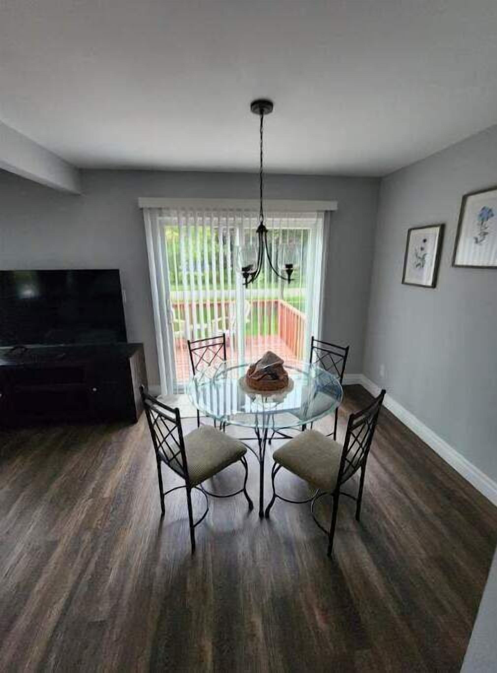 Un coin repas avec une table et des chaises en verre, un lustre et un téléviseur posé sur un meuble.