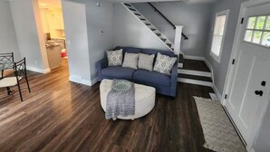 Ein Wohnzimmer mit einem blauen Sofa, gemusterten Kissen, einem runden Hocker und einer Treppe, die zu einer anderen Ebene führt.