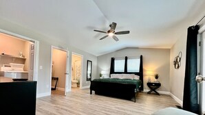 Una habitación amplia con cama, ventilador de techo, una mesita de noche con lámpara y una silla.