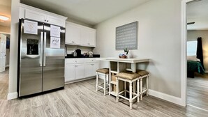 Una cocina moderna con un refrigerador de acero inoxidable, gabinetes blancos y una barra con taburetes.