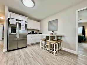 A modern kitchen with a stainless steel refrigerator, white cabinets, and a bar area with stools. - New remodel exquisite master suite Trenton, Ohio (Trenton)