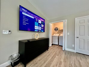 A room with a flat-screen TV mounted on the wall displaying a streaming service interface, a black dresser, a laundry basket, and a door leading to another room. - New remodel exquisite master suite Trenton, Ohio (Trenton)