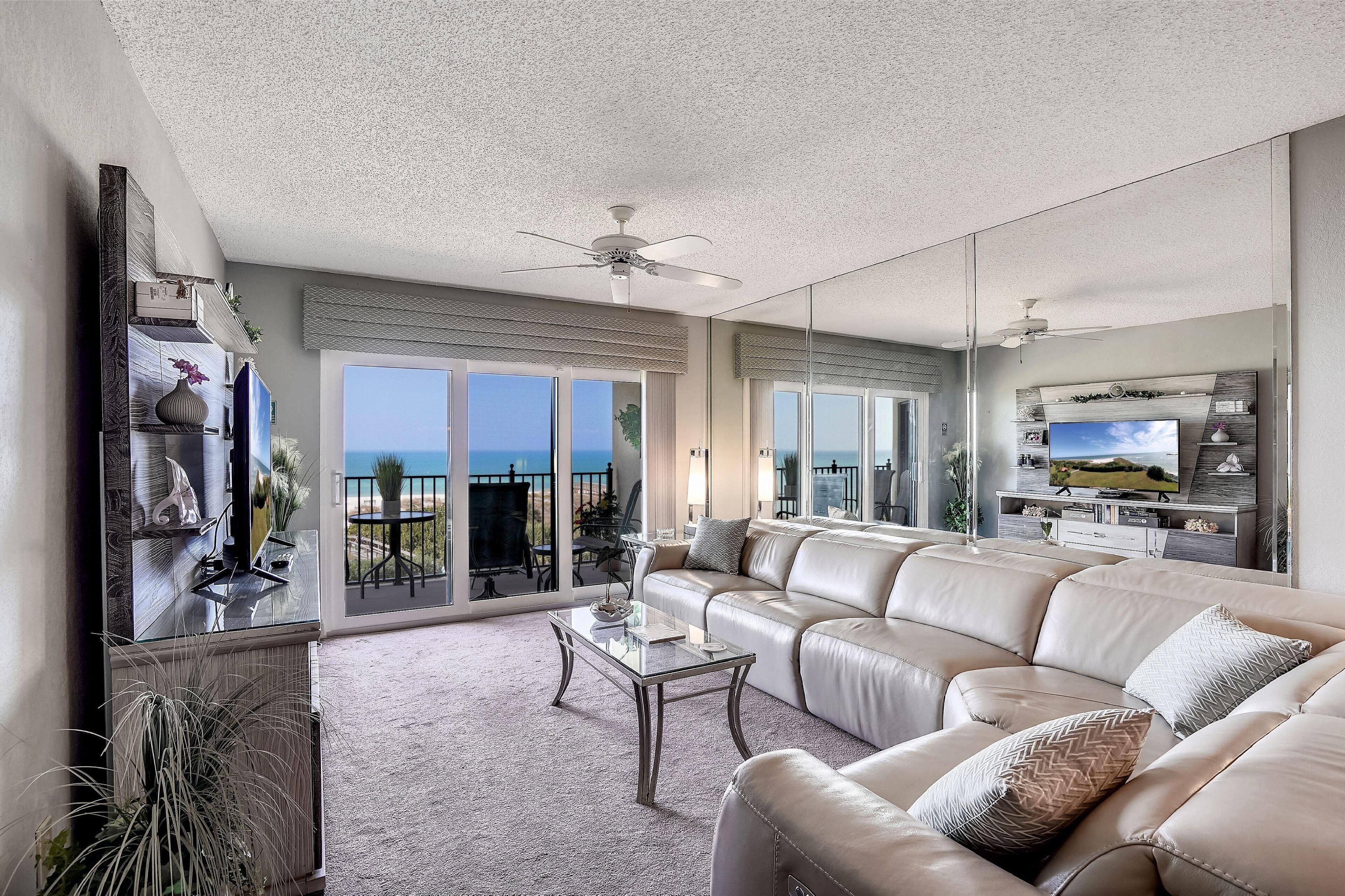 Een ruime woonkamer met een grote bank, een salontafel en een televisie. Er is een balkon met uitzicht op de oceaan.
