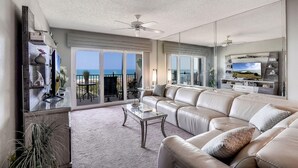 A spacious living room with a large sofa, a coffee table, and a TV. There is a balcony with a view of the ocean. - Land's End 6-404 Beach Front (Treasure Island)