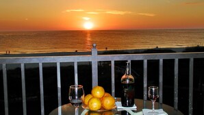 A sunset view from a balcony with a table featuring oranges, wine glasses, and a bottle. - Land's End 7-202 Beach Front (Treasure Island)