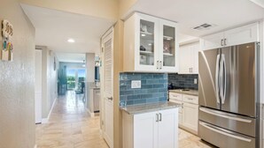 A modern kitchen with white cabinets, a stainless steel refrigerator, and a blue tiled backsplash. - Land's End 7-203 Beach Front - Premier (Treasure Island)