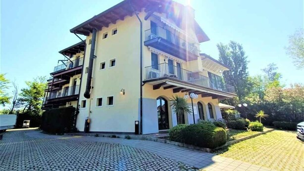 A multi-story building with balconies, a paved driveway, and surrounding greenery.