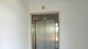 A narrow hallway with a closed elevator door, white walls, and tiled flooring.