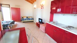 A room with a bed, a TV, a red kitchen, and a window.