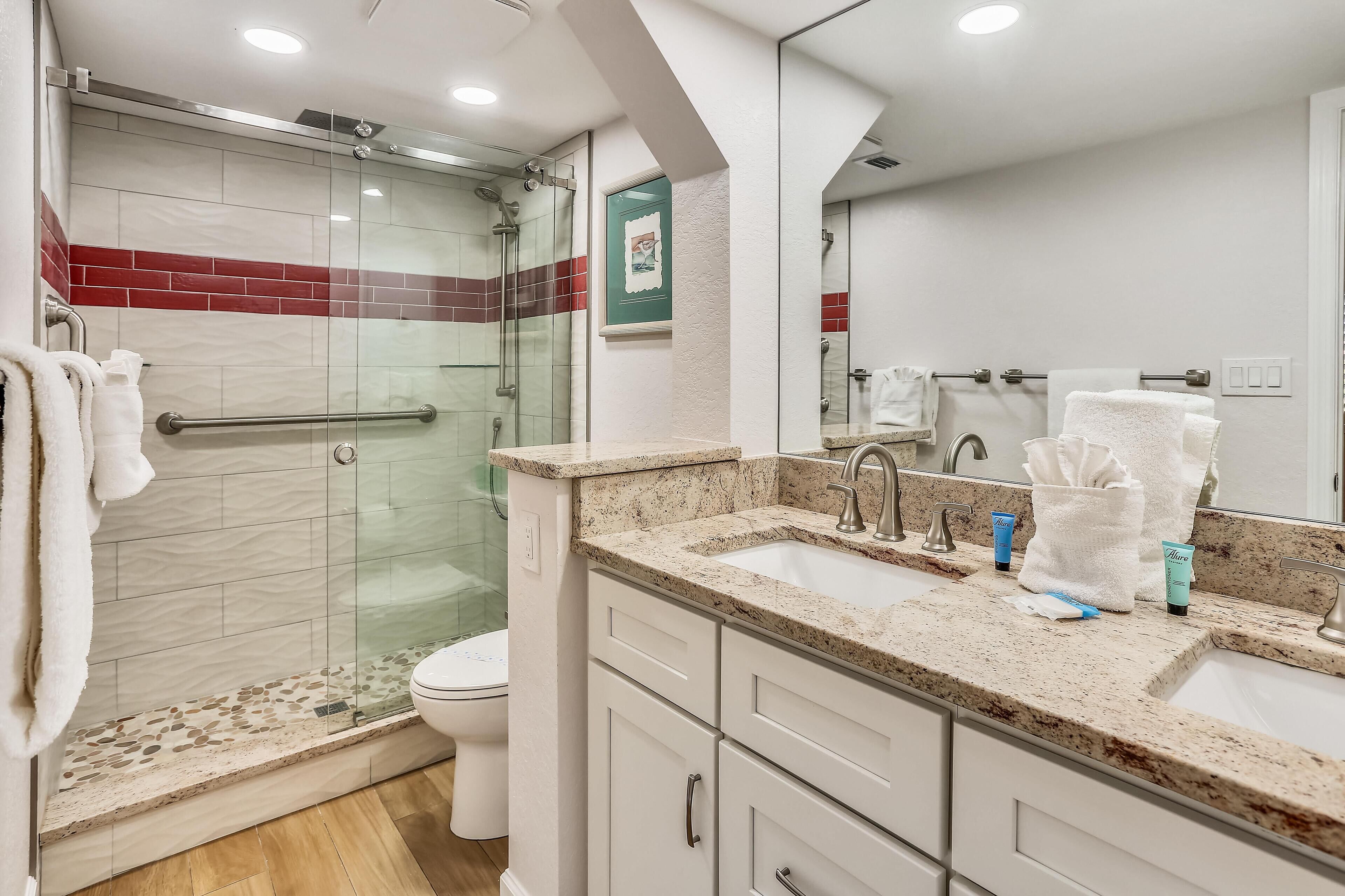 A modern bathroom with a glass shower enclosure, a sink with a marble countertop, and a toilet.