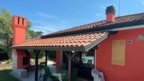 A red building with a tiled roof, a chimney, and a patio area with green chairs and a table.