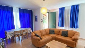 A living room with a sofa, a coffee table, a dining table with chairs, and blue curtains.