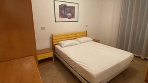 A bedroom with a bed, a wooden headboard, a nightstand, a framed picture on the wall, and a window with curtains.