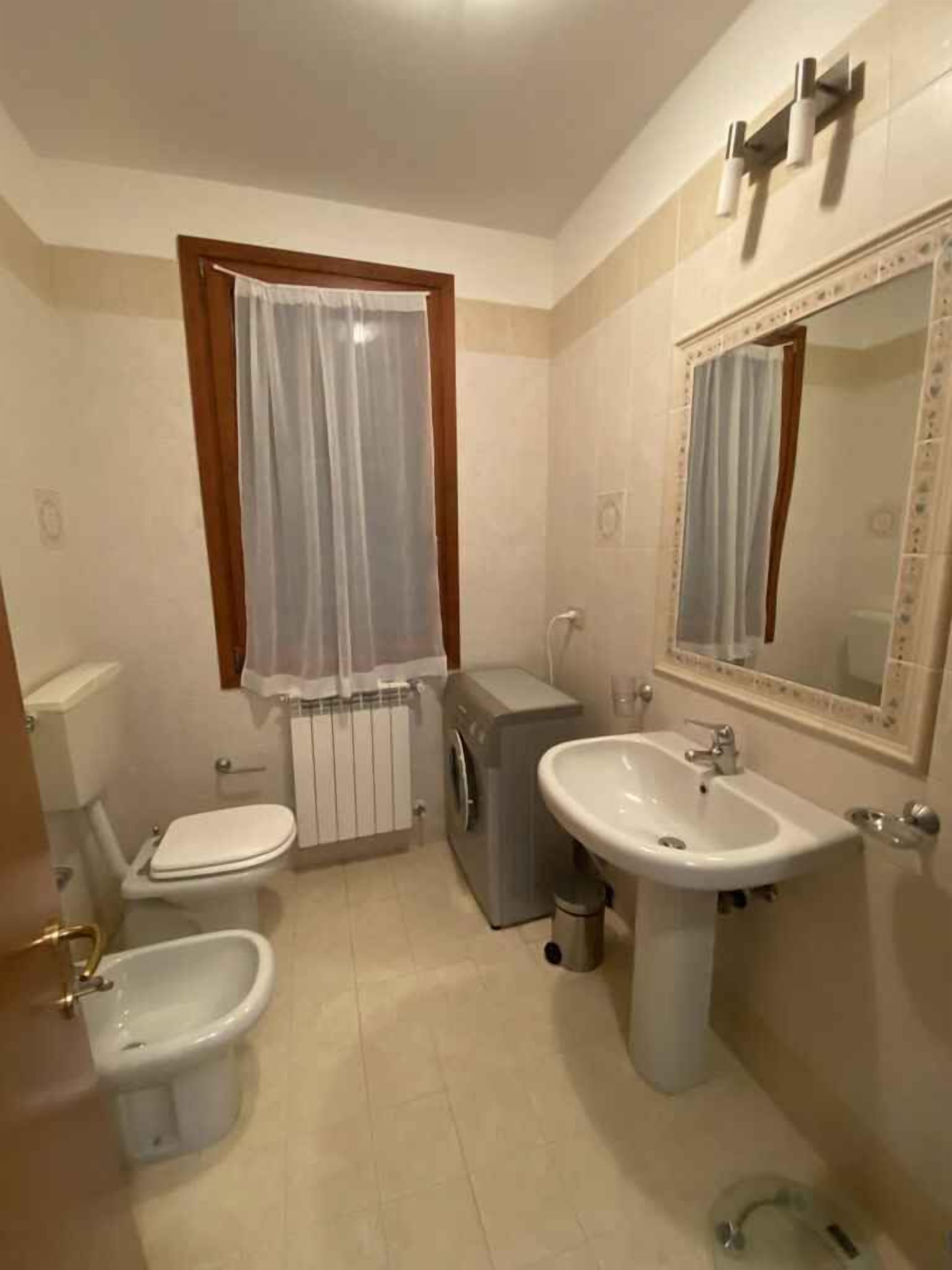 A bathroom with a toilet, bidet, washing machine, sink, and mirror.
