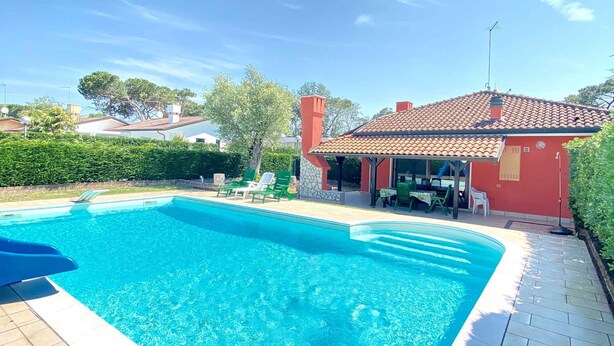 A swimming pool with lounge chairs, a red building with a tiled roof, and a clear blue sky.