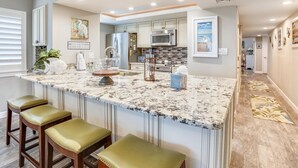 A kitchen with a marble island, bar stools, and a view into the dining area. - Land's End 7-306 Beach Front - Premier (Treasure Island)