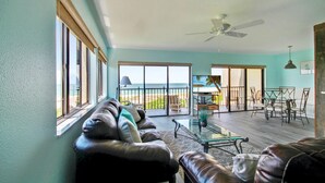 A spacious living area with a view of the beach, a ceiling fan, and a dining area with chairs and a table. - Land's End 7-401 Beach Front - Premier (Treasure Island)