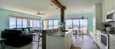 Una cocina amplia con una isla grande, armarios blancos y vistas al océano.