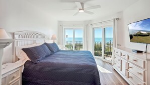 A bedroom with a bed, a TV, a ceiling fan, and a balcony with a view of the sea. - Land's End 7-402 Beach Front - Premier (Treasure Island)