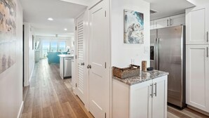 A modern kitchen with white cabinets, a stainless steel refrigerator, and a wooden floor. - Land's End 7-402 Beach Front - Premier (Treasure Island)