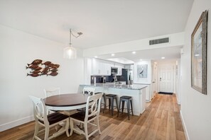 A modern kitchen with white cabinets, a central island, and a dining area with a round table and chairs. - Land's End 7-402 Beach Front - Premier (Treasure Island)