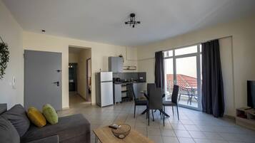 A modern living room with a sofa, a coffee table, and a dining area with chairs. There is a kitchen in the background, and a balcony with a view.